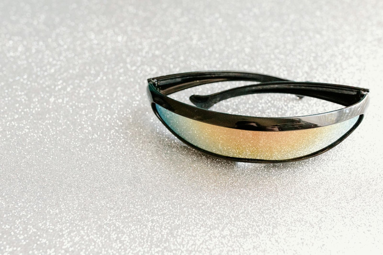 Close-up of futuristic sunglasses featuring reflective multicolored lenses on a sparkling background.