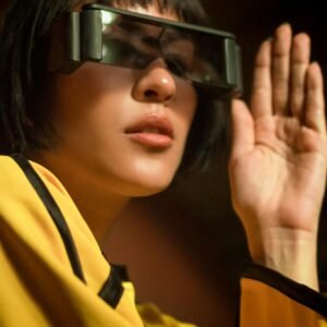 Woman wearing futuristic sunglasses and a yellow outfit, posing indoors with a trendy vibe.